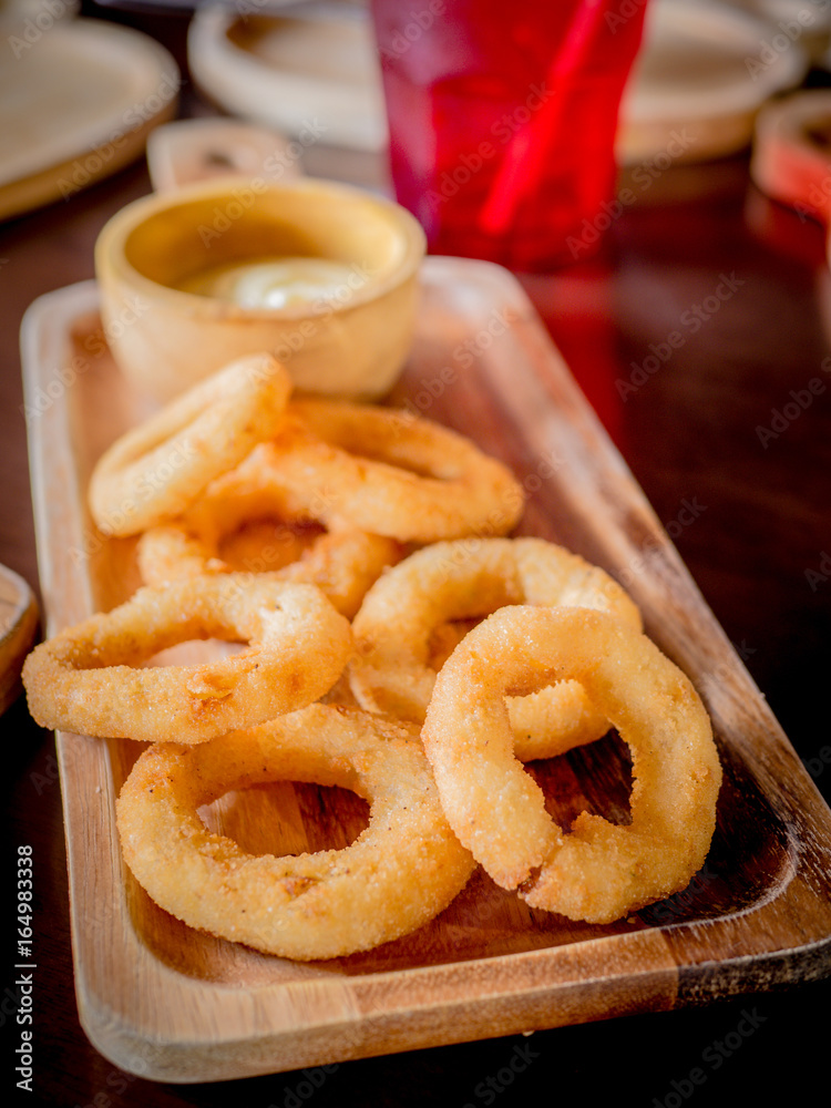 Fried breaded onion rings with sauce on a classic wooden plate. Fried breaded onion rings with sauce on a classic wooden plate.