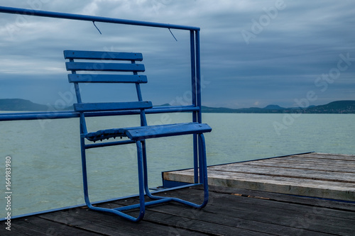 blue metal chair on wooden pier at Balaton lake - lonely day  windy and cloudy weather in the summer season