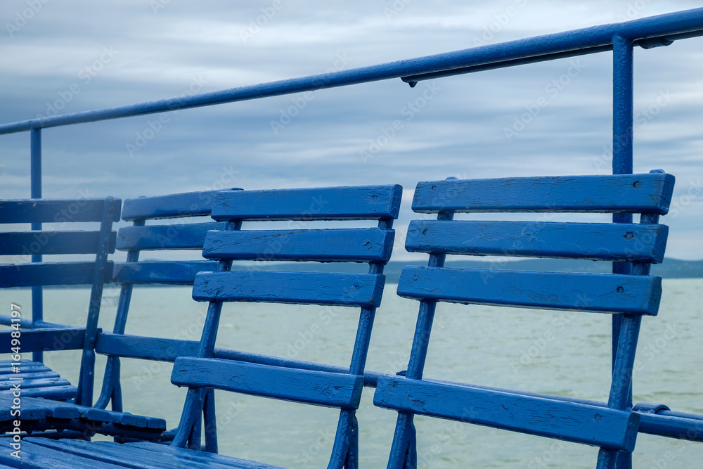 blue chairs on dock or pier waiting for turist - cloudy sky cold weather at Balaton lake in the summer season blue chairs on dock or pier waiting for turist - cloudy sky cold weather at Balaton lake in the summer season