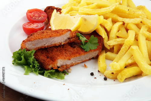 Dish of Wiener schnitzel and French fries served with sauces and salad on rustic wooden table