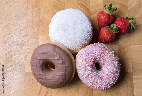 Strawberry, chocolate and jam donuts on a wooden background with strawberries