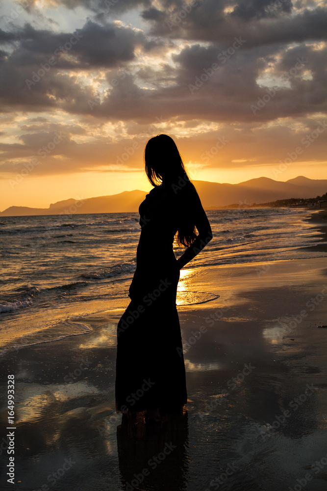 Silhouette of a beautiful woman on the background of the sea at sunset.