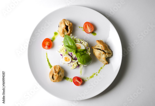 Salad with pies and lettuce leaves on a white plate