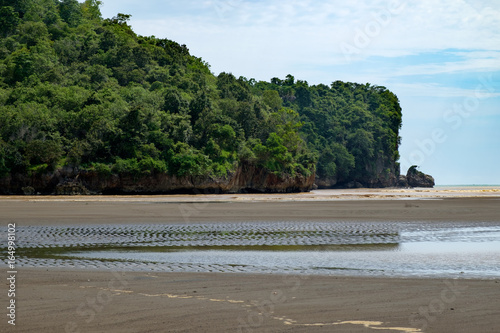 tropical paradise at low tide - brown sand shore with cloudy sky and green cliffs in background at Pacitan beach, Java island, Indonesia