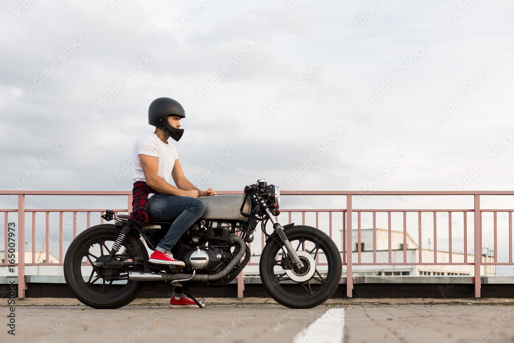 Handsome happy rider man in red sneakers, white t-shirt and black moto  helmet sit on