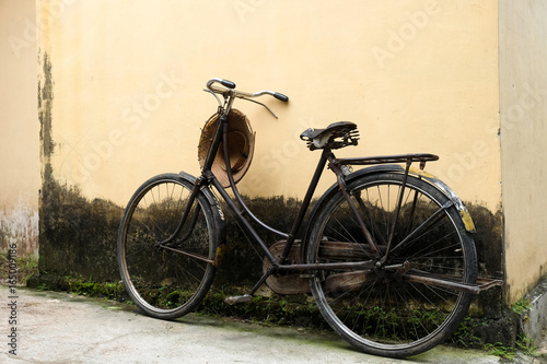 my grandpa's lifestyle - raised old black bycicle against a yellow mossy wall with rice field worker hat