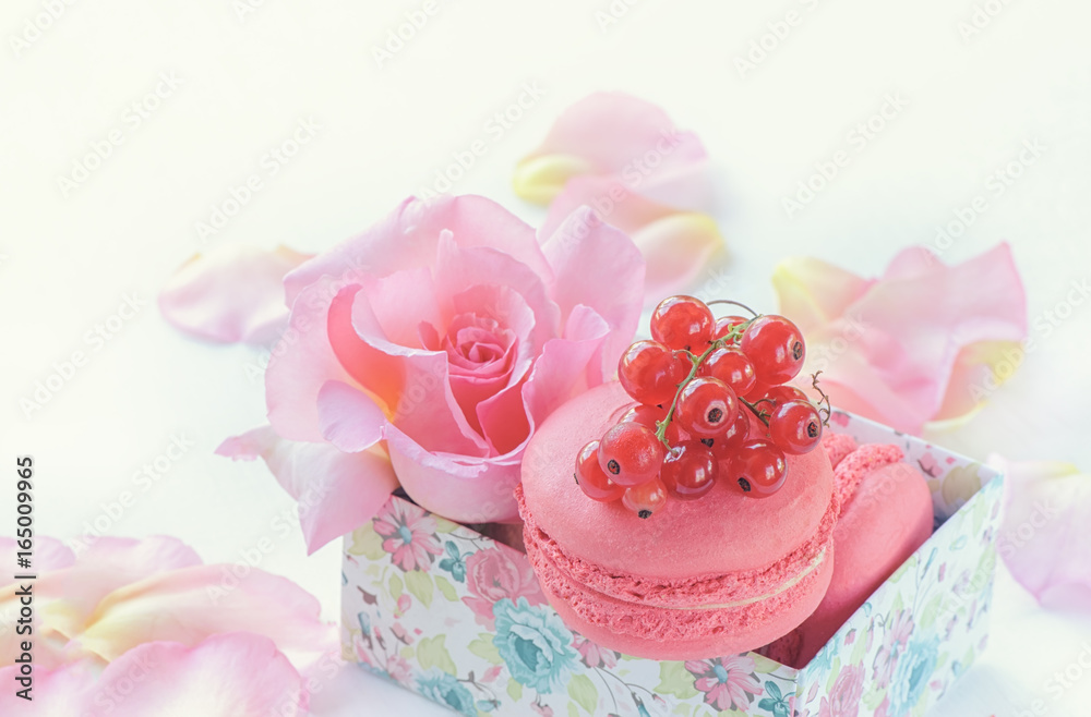 Macaroni, red currants, marshmallows against the background of beautiful flowers of roses. Dessert closeup.