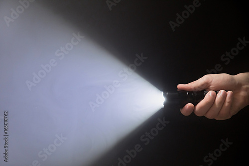 Black flashlight with a beam of light in male's hand isolated from right side of the frame on black background copyspace photo
