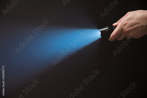 Male hand holding a led flashlight with a narrow blue beam on a black background, leaving the right side of the frame