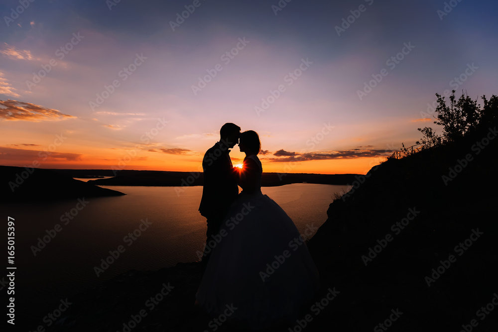 Silhouette of embracing groom and bride. Tenderly kissing weddin