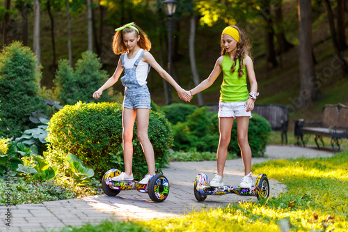 Happy girls riding on hover boards or gyroscooters outdoors at sunset in summer. Active life concept photo