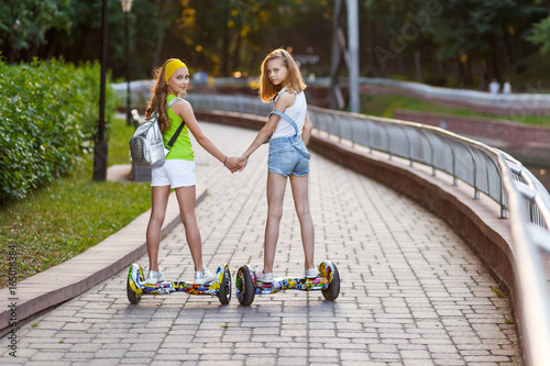 Happy girls riding on hover boards or gyroscooters outdoors at sunset in summer. Active life concept photo