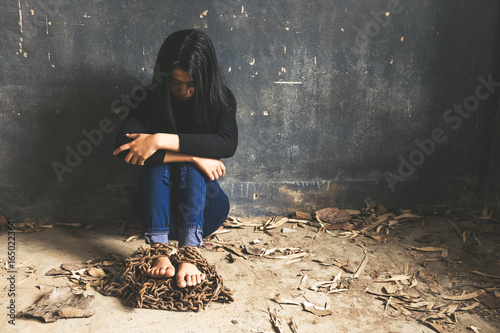 Trapped woman. Young woman trapped in chains covering face with hands while sitting on the floor in a dark room