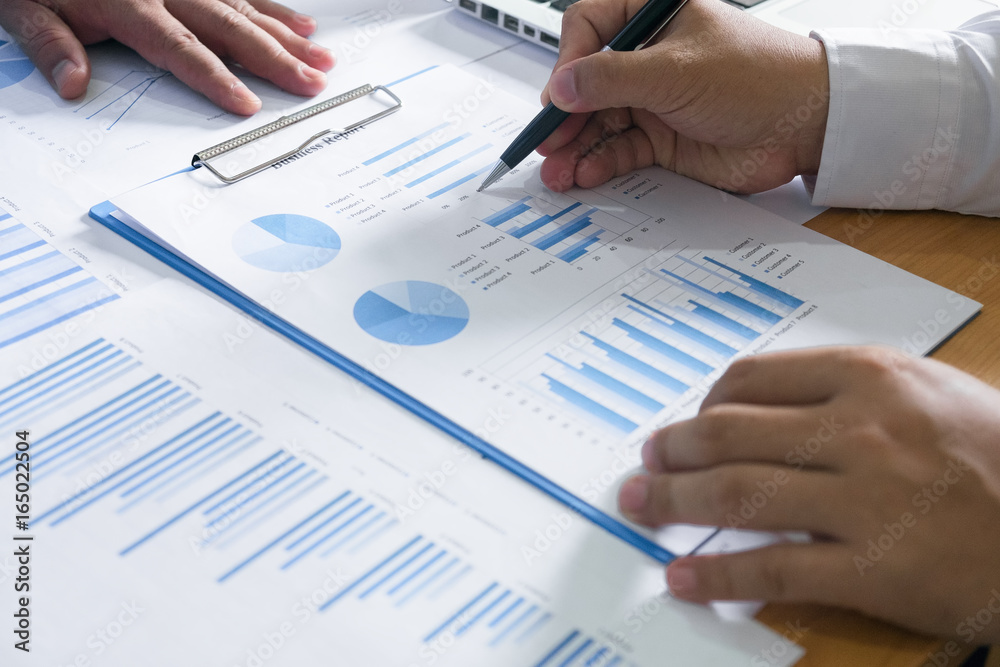 Business people brainstorming at office desk, they are analyzing financial reports and pointing out financial data on a sheet Business people brainstorming at office desk, they are analyzing financial reports and pointing out financial data on a sheet