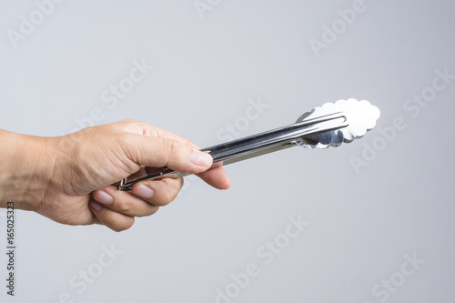 Hand holding silver serving kitchen tongs for picking food photo