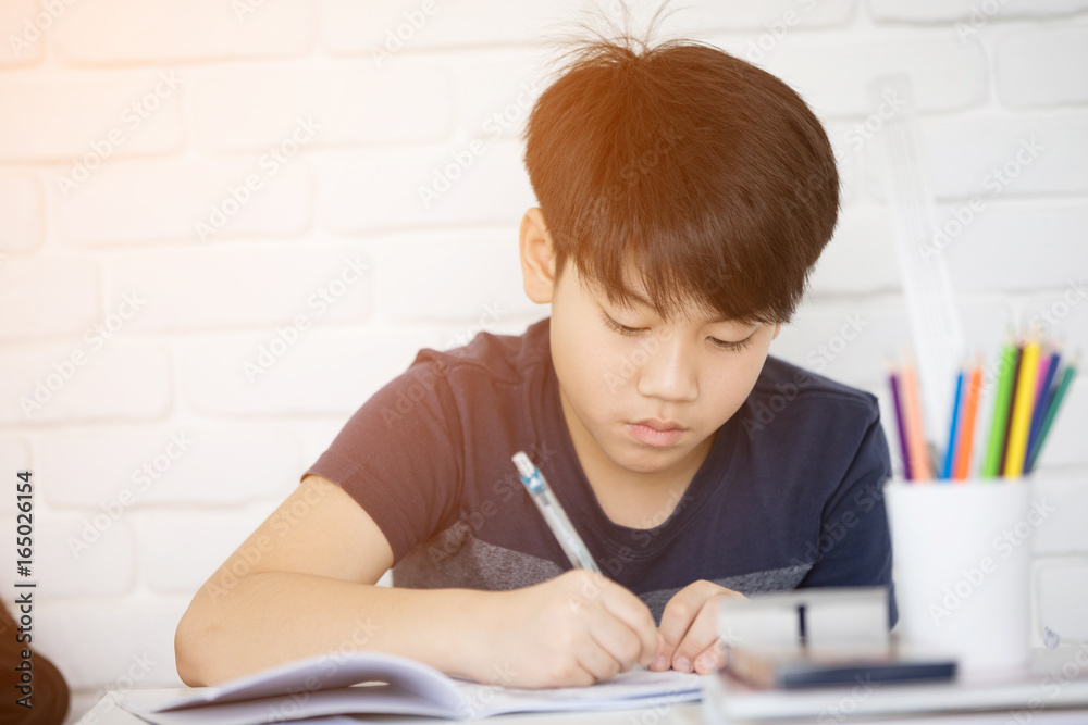 Asian boy doing homework near white brick wall Asian boy doing homework near white brick wall