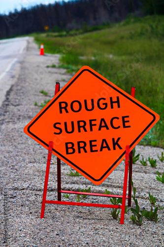 An orange rough surface break sign with construction pylons behind it