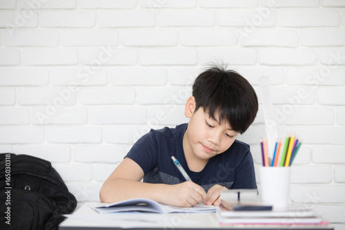 Asian boy doing homework near white brick wall