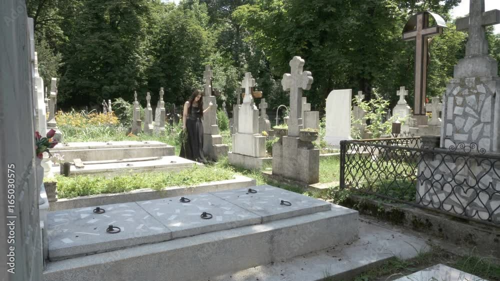 Funeral gothic girl walking beside tombstones in ancient graveyard contemplating death and solitude Funeral gothic girl walking beside tombstones in ancient graveyard contemplating death and solitude