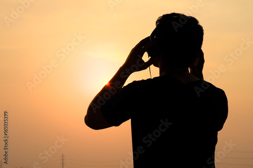 Man silhouette listening to the headphones on the sunset landscape background
