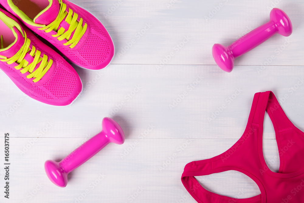 Women's sportswear, with pink dumbbells, on a light wooden floor Women's sportswear, with pink dumbbells, on a light wooden floor