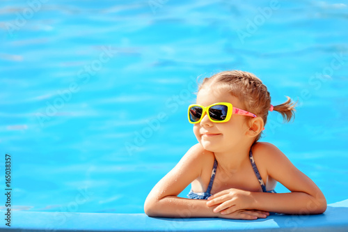 Tela Smiling cute little girl in sunglasses in pool in sunny day.