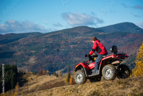 Male on an ATV riding down the hilly road on a background of mountains, forest and blue sky. The concept of an active holiday in the mountains