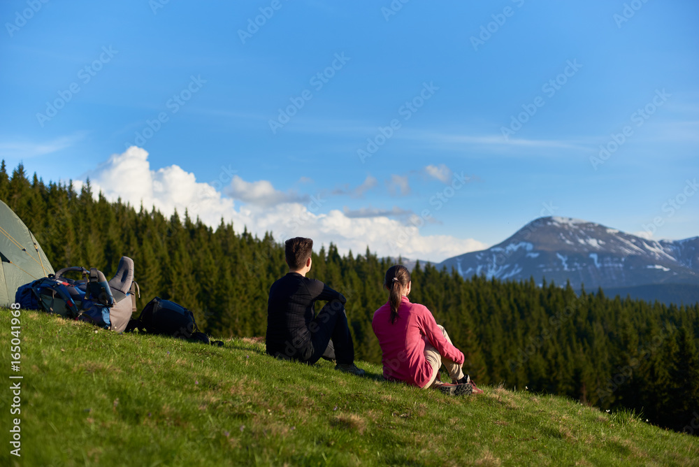 Fototapeta premium Rearview shot of two women sitting on top of a hill near their tent enjoying beautiful mountains view copyspace lifestyle activity sport health friendship travelling