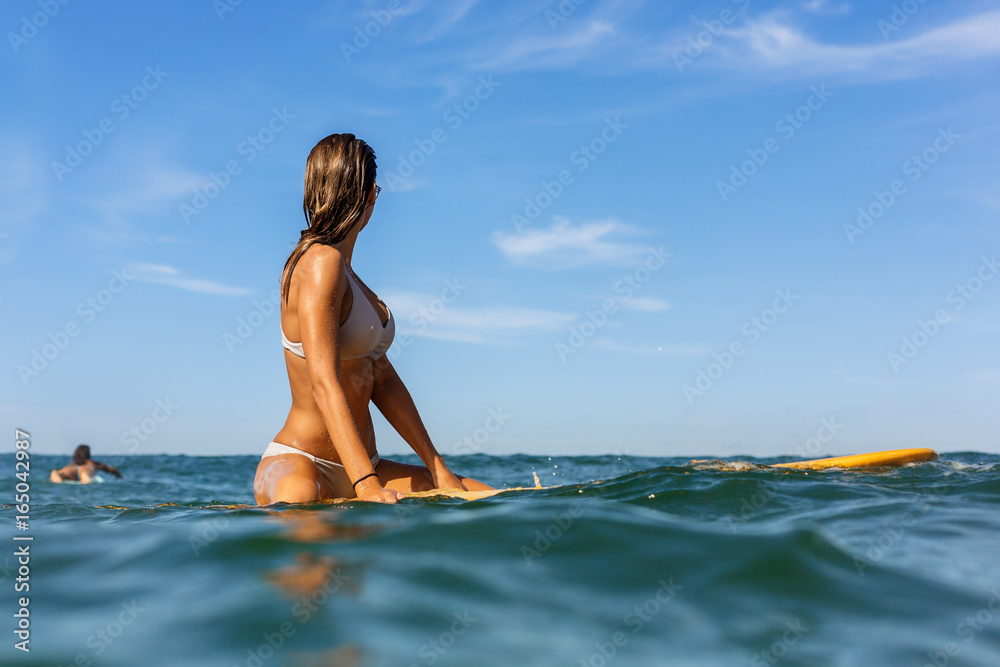 Two beautiful fit surfing girl in sexy bikini on surf surfboard board on sunrise or sunset in the ocean. Woman look how her friend swim in open sea. Modern active sport lifestyle and summer vacation.