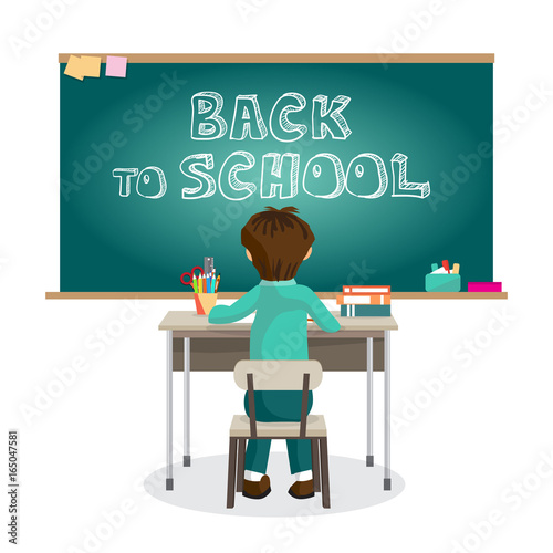 Boy is sitting on the first desk at the blackboard in primary sc