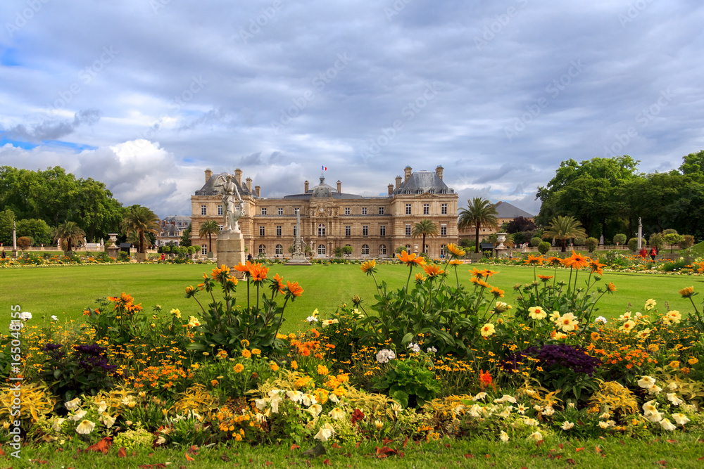 Jardin du Luxembourg with the Palace and statue. Few flowers are in front and blue sky behind.