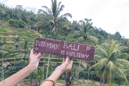 Wooden nameplate with text everyday Bali is holiday in the woman hands on a tropical rice terrace background of Bali island of parardise, Indonesia. photo