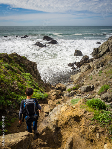 10 year old boy hiking on California Coast down to beach with crashing waves, Pirates Cove Trail, Marin Headlands, Golden Gate National Recreation Area, California, United States