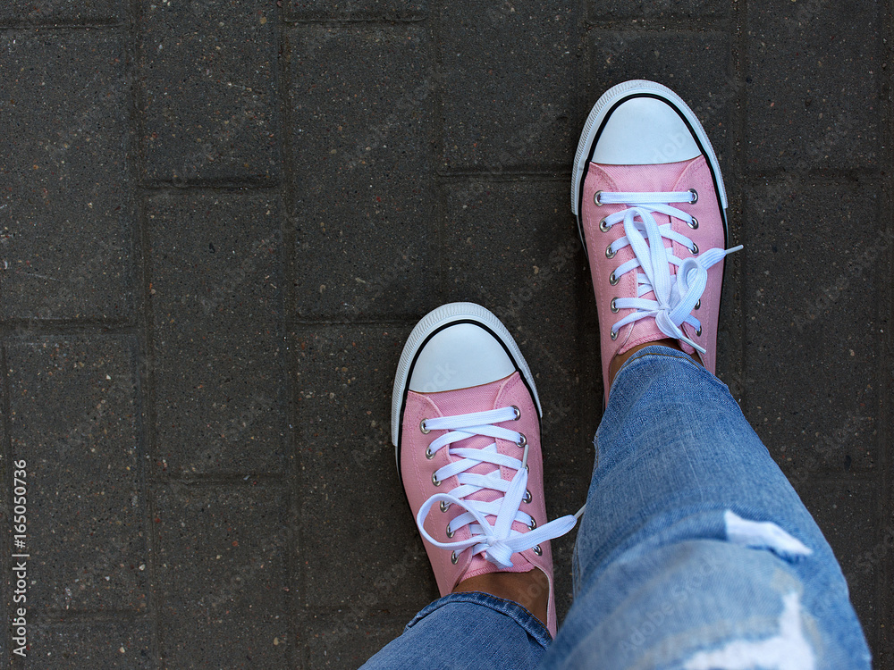 Pink sneakers for the girl on her feet against the backdrop of the road