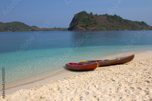 Kayaks on the beach with beautiful crystal clear blue sea and island in the background © Pattara