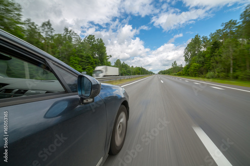 The car moves at high speed on highway at the sunny summer day.