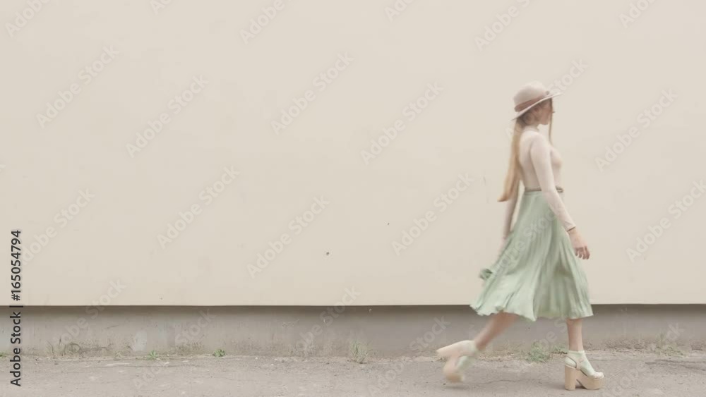 Model in a hat and a long skirt walks on the camera against the wall Model in a hat and a long skirt walks on the camera against the wall