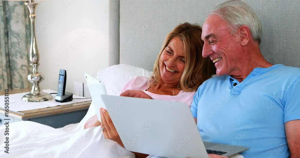 Happy senior couple on bed using laptop and digital tablet Happy senior couple on bed using laptop and digital tablet