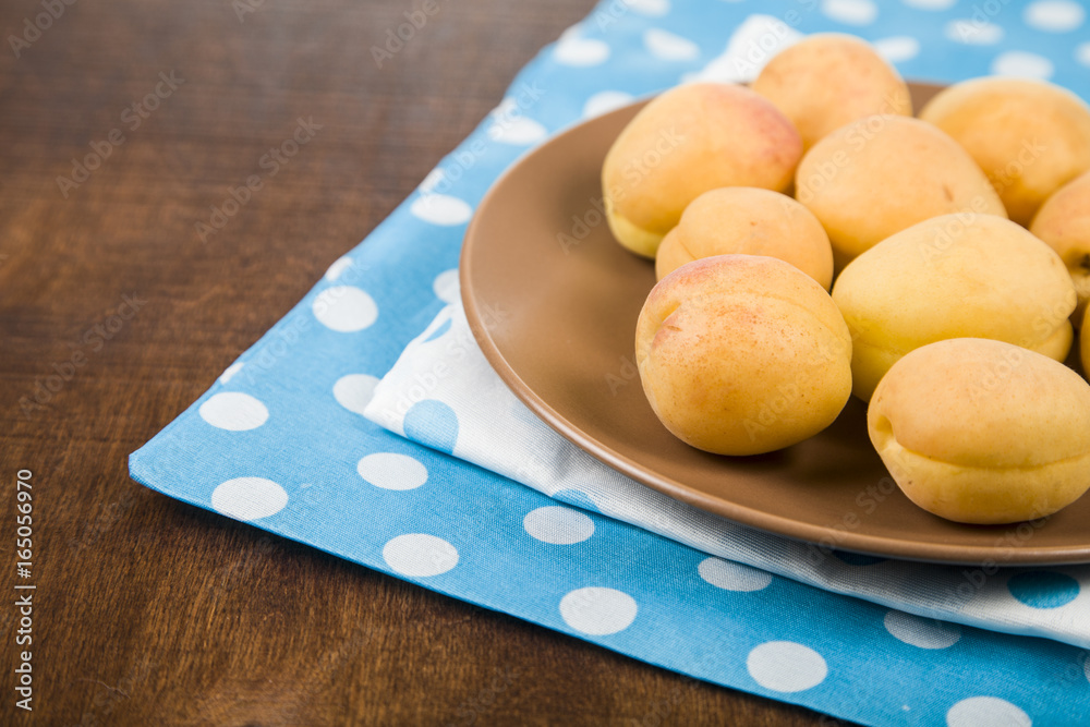 Apricots in a plate on a wooden table.