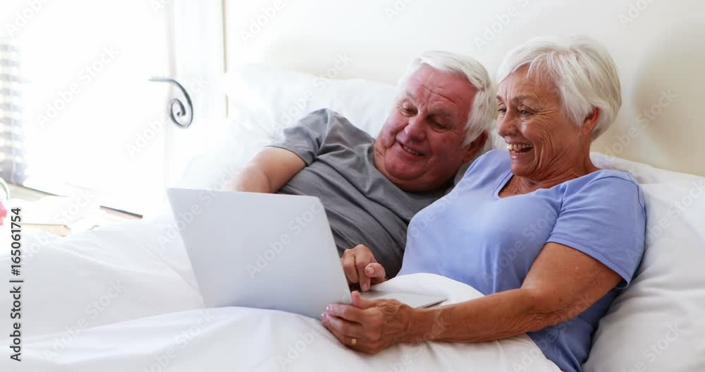Happy senior couple using laptop on bed Happy senior couple using laptop on bed