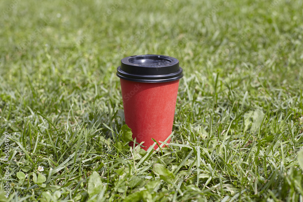 Red paper cup of coffee to takeaway on green grass lawn. Breakfast morning outside the cafe Red paper cup of coffee to takeaway on green grass lawn. Breakfast morning outside the cafe