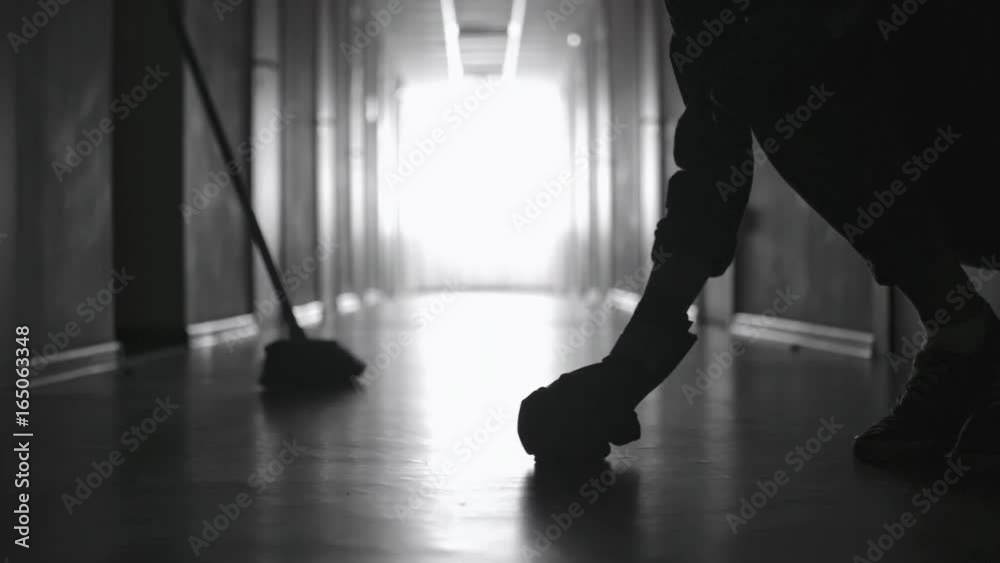 PAN with low-section of silhouette of legs of unrecognizable cleaner scrubbing floor in dark corridor  