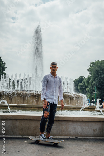 Young handsome man (20-25) posing in front of a water fountain with a skateboard