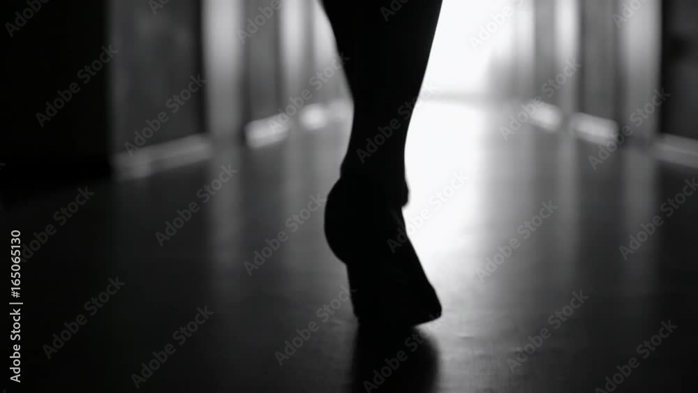 Tracking with low-section of silhouette of female legs in high heels shoes walking along dark hallway; black and white slow motion shot Tracking with low-section of silhouette of female legs in high heels shoes walking along dark hallway; black and white slow motion shot