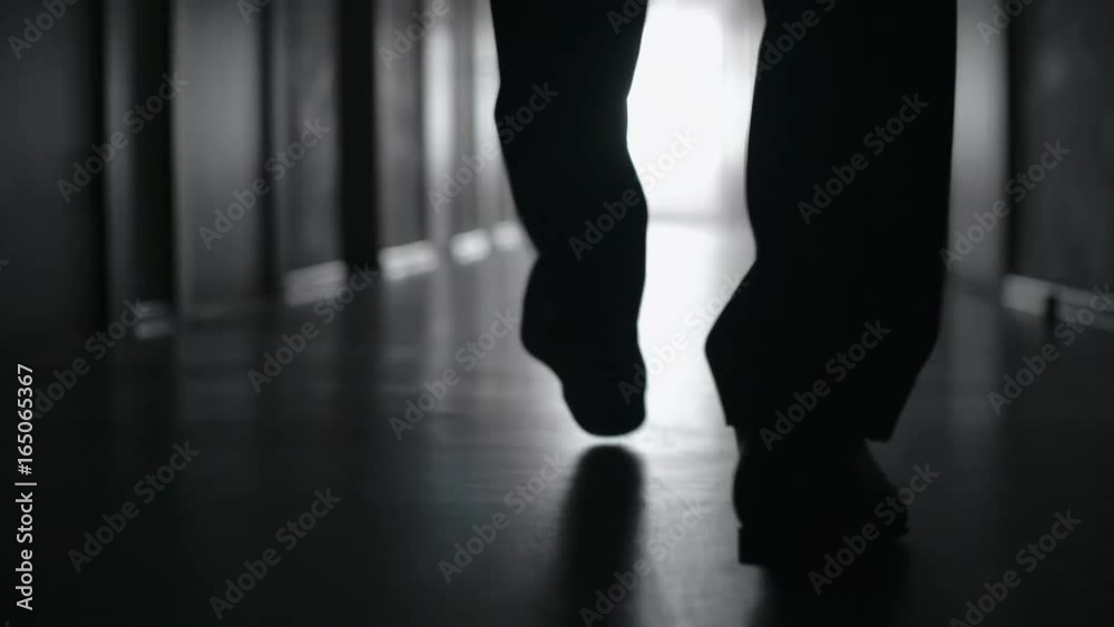 Tracking with low-section of silhouette of legs of businessman walking along corridor in slow motion