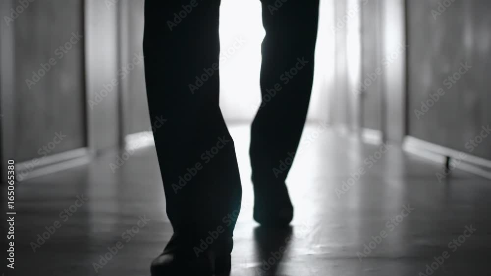 Dolly with low-section of silhouette of legs of man walking along hallway in slow motion; black and white shot Dolly with low-section of silhouette of legs of man walking along hallway in slow motion; black and white shot