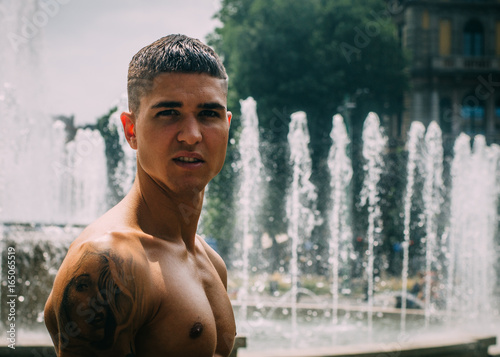 Athletic young man  20-25  looking straight at camera with fountain in background