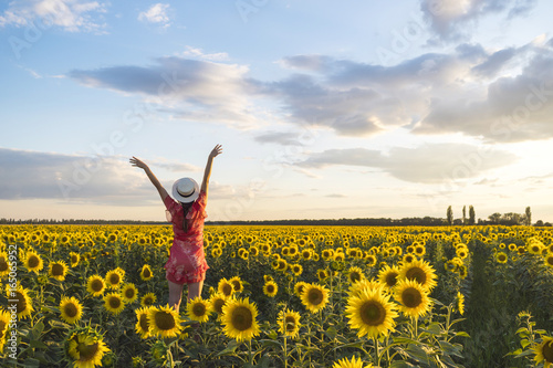 Sunflower on in the field and a young girl in a red dress with arms raised