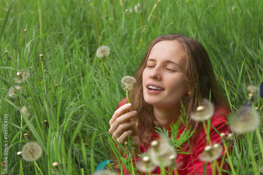 Portrait of the attractive woman in the grass considering a dandelion flower
