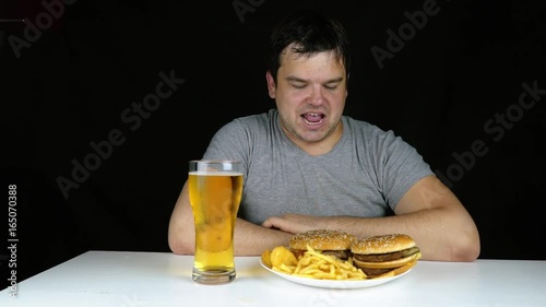 Diet failure of fat man eating fast food hamberger. Happy smile overweight person who spoiled healthy food by eating huge hamburger on fork. Junk meal leads to obesity. Refusal from harmful food. photo